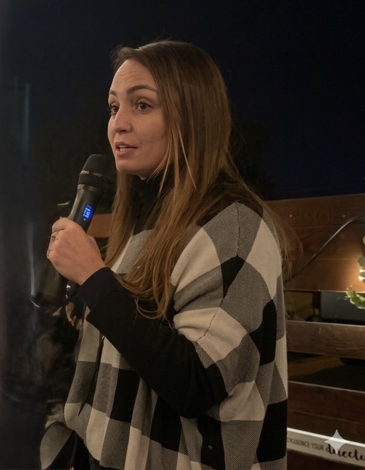 Danielle Vantini speaking with microphone — checkered outfit